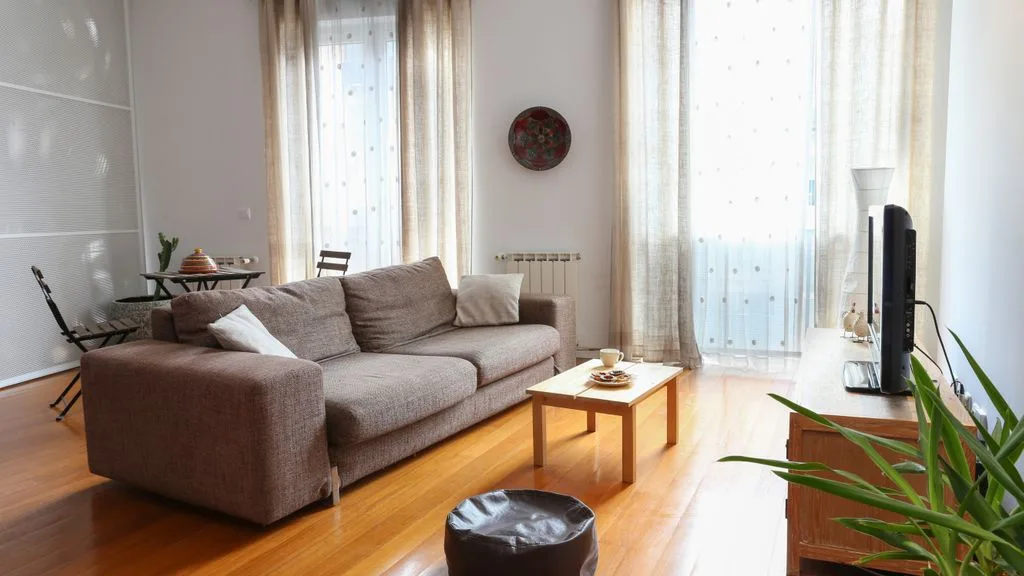 Una sala luminosa con asientos, una mesa de centro y ventanas altas con cortinas.