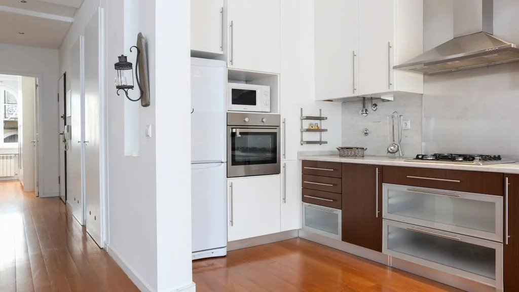 Una cocina moderna con armarios blancos, muebles inferiores oscuros y electrodomésticos integrados.