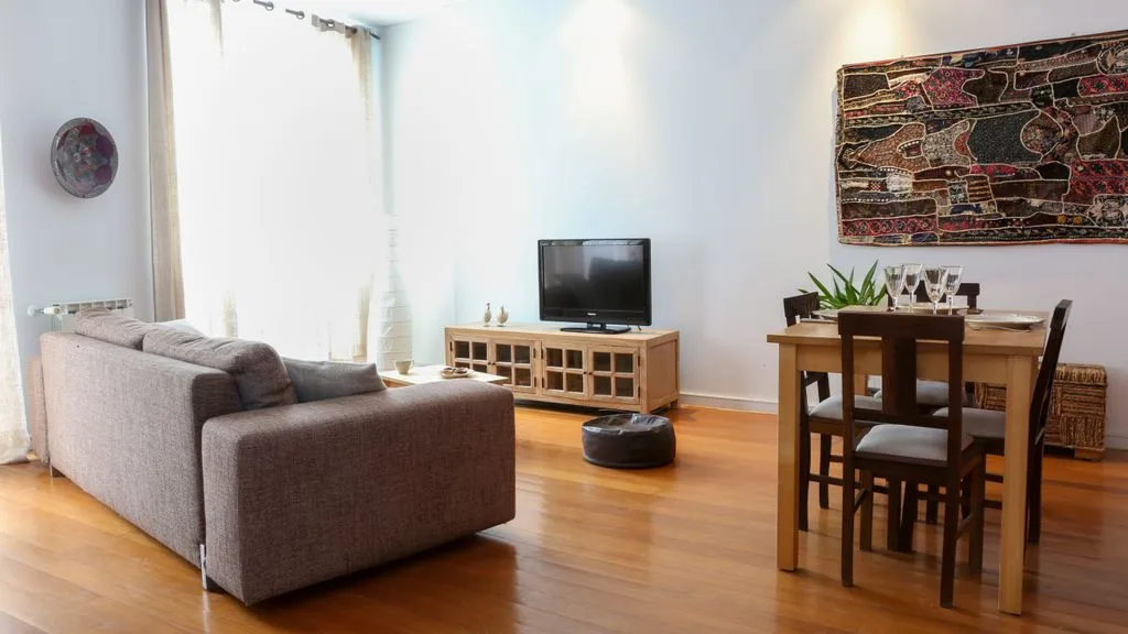 Zona de estar y comedor con asientos, un televisor y una mesa de madera.