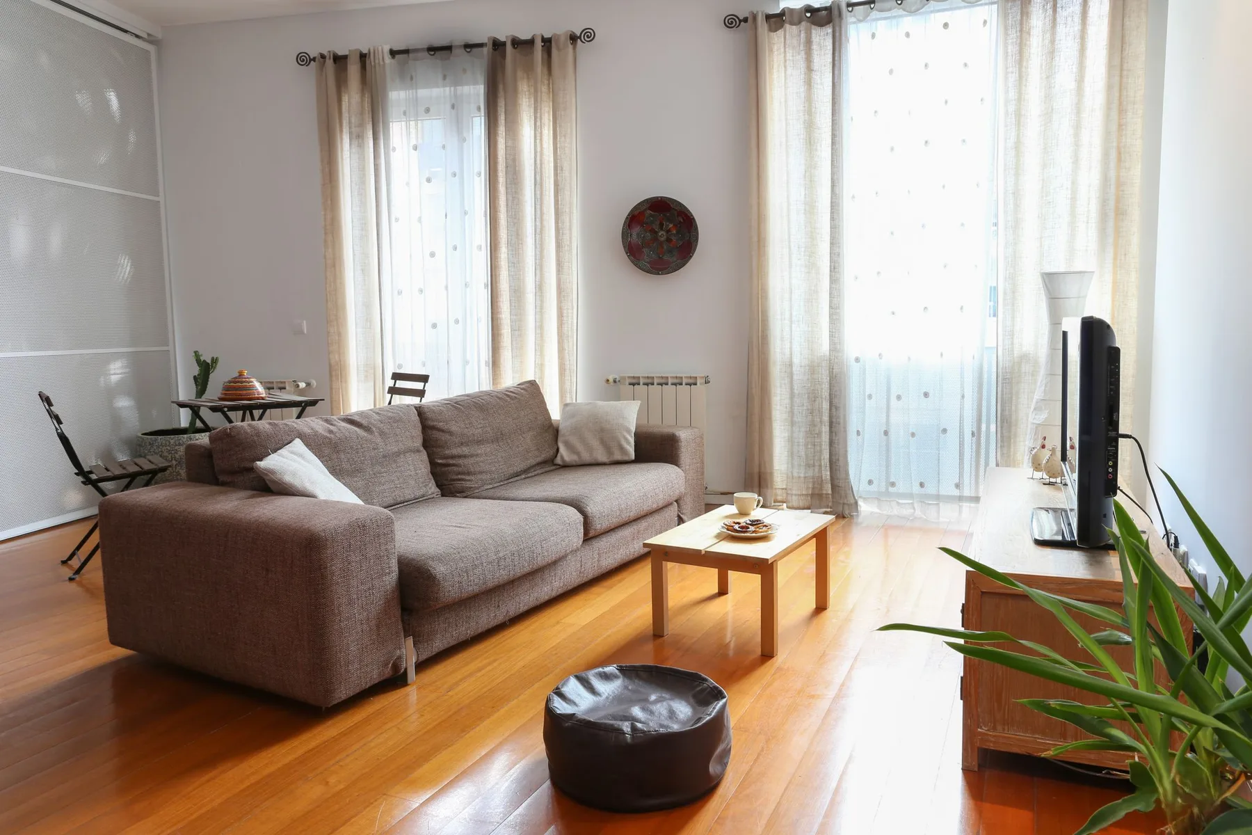 Una sala luminosa con un sofá seccional y ventanas altas con cortinas.