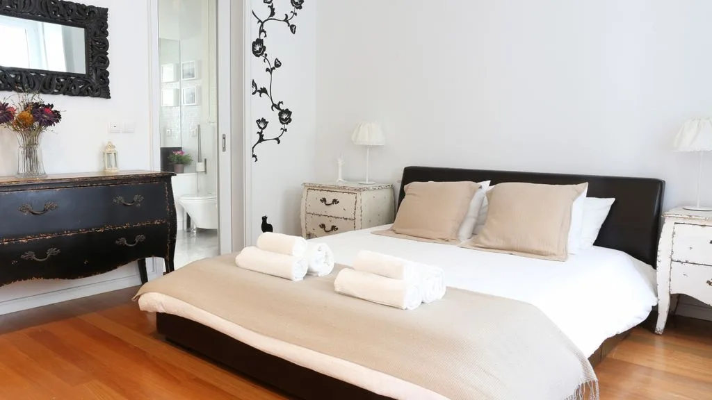 Un dormitorio luminoso con una cama grande, mesitas de noche y suelo de madera.