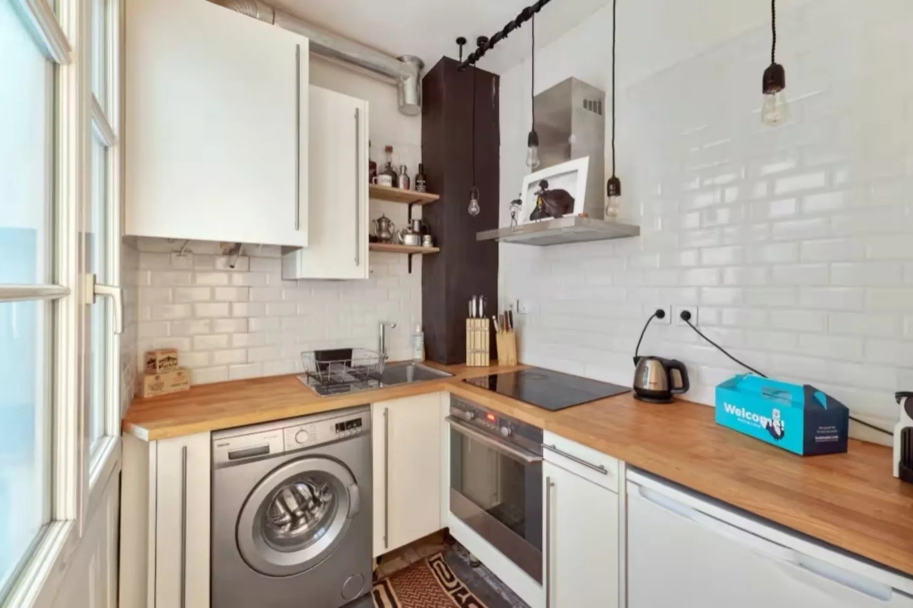 A compact kitchen with white cabinets, wooden counters, and a washing machine.