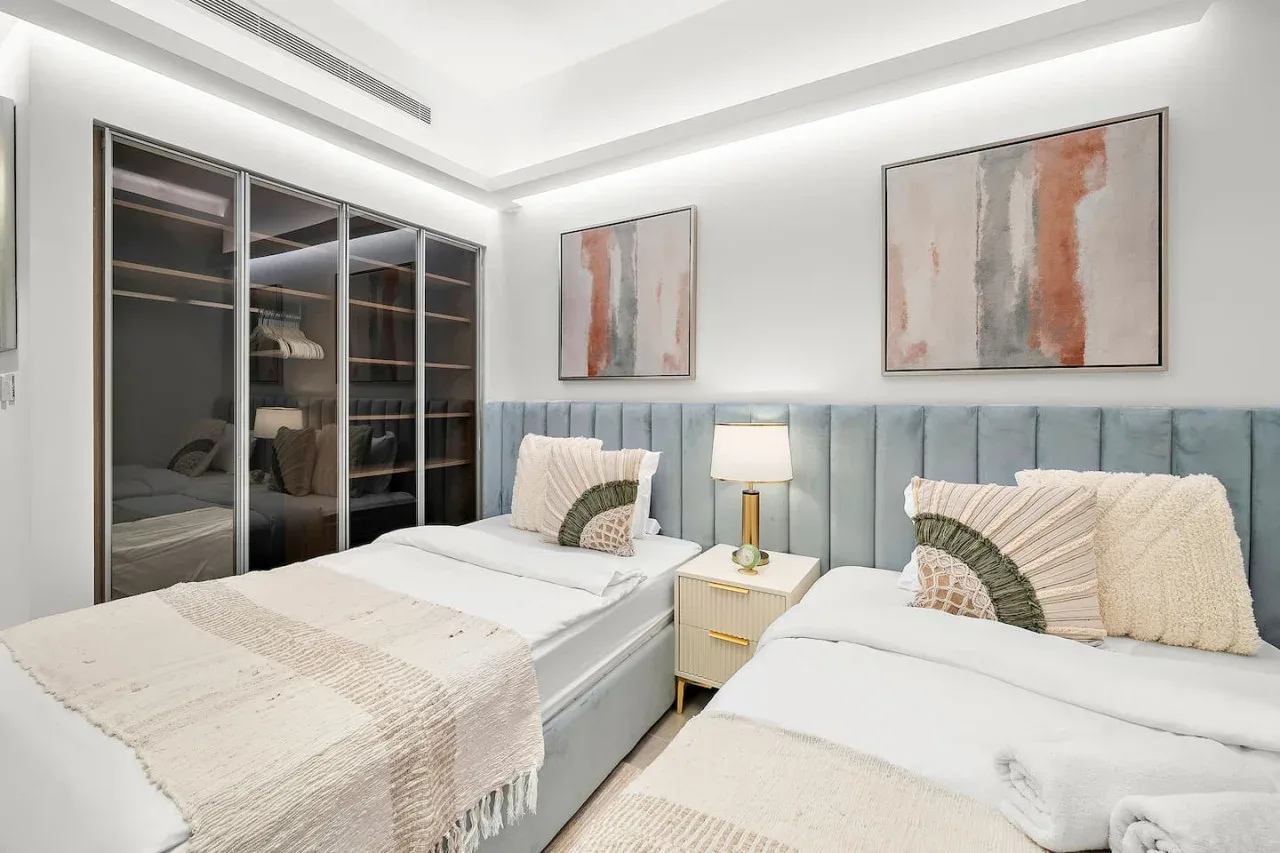 Un dormitorio luminoso con dos camas y cuadros abstractos en las paredes.