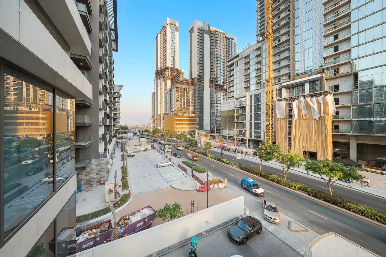 Una calle urbana transcurre entre edificios modernos de gran altura bajo un cielo despejado.