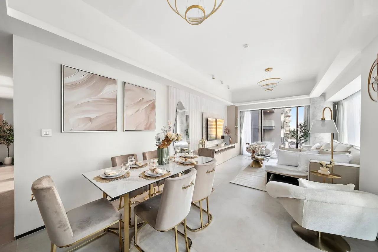 Un luminoso espacio abierto de comedor y sala de estar con una mesa y asientos junto a grandes ventanas.