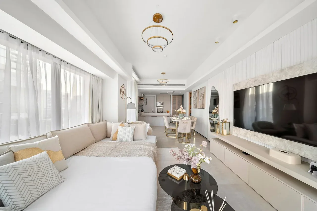 Una sala luminosa con asientos, un televisor y un comedor al fondo.