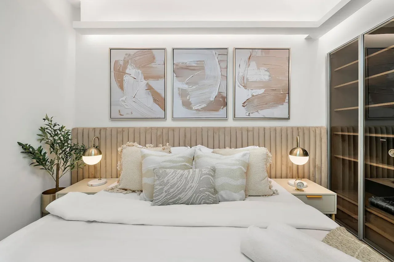 Un dormitorio con una cama bien tendida bajo tres cuadros abstractos enmarcados.