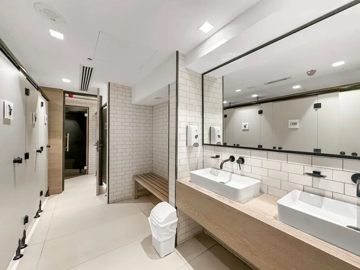 Un baño revestido de azulejos con una encimera larga, dos lavabos y un banco.