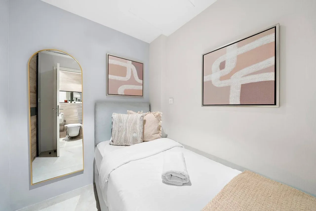 Dormitorio con ropa de cama blanca, cojines decorativos y arte abstracto en las paredes.