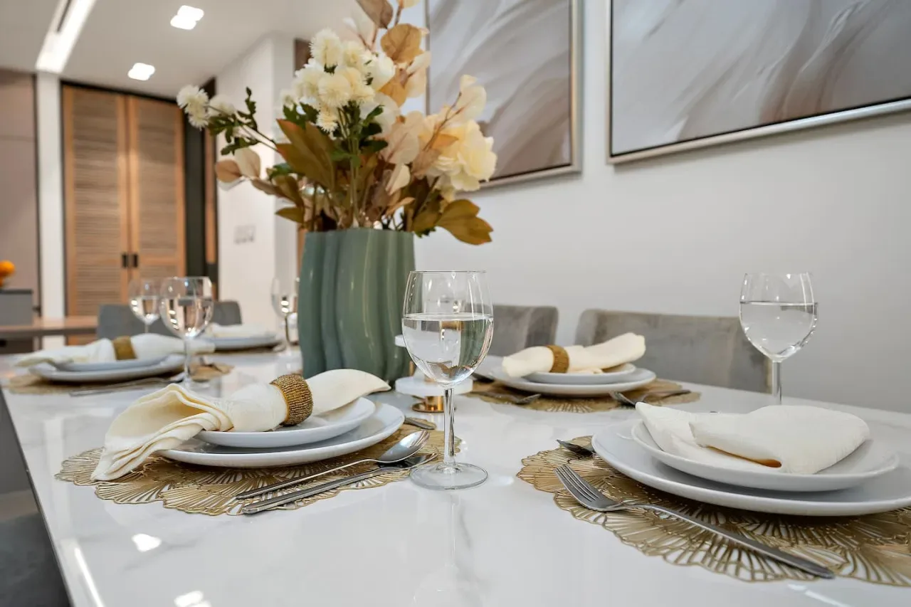 Una mesa de comedor está preparada con platos, copas y un jarrón de flores.
