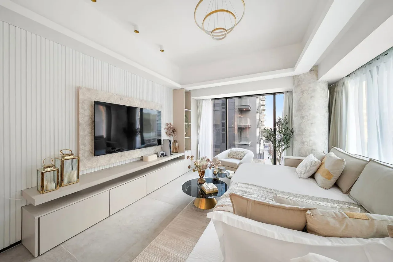 Una sala luminosa con televisor y asientos junto a grandes ventanales.
