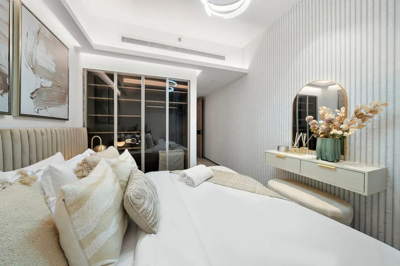 Un dormitorio luminoso con una cama, cuadros enmarcados y un tocador flotante.