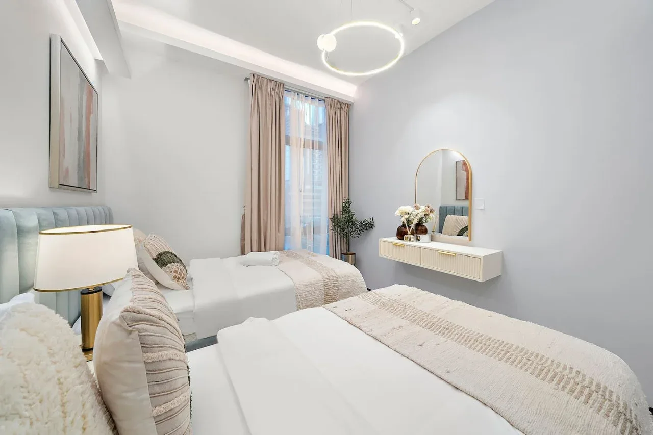 Un dormitorio luminoso con dos camas, una ventana y un tocador flotante.