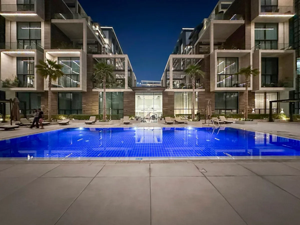 Una piscina iluminada se encuentra entre edificios de apartamentos modernos por la noche.