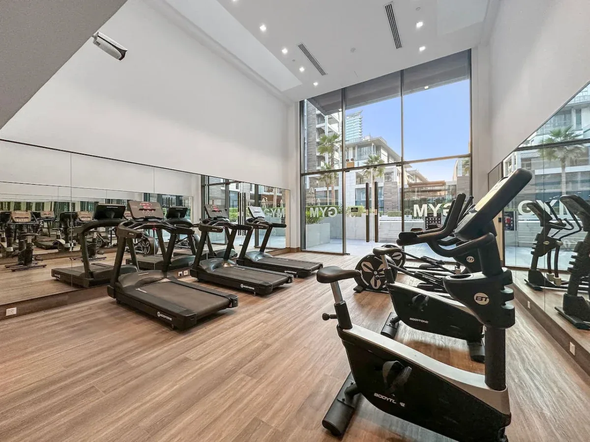Un gimnasio luminoso con cintas de correr, bicicletas estáticas y ventanales.
