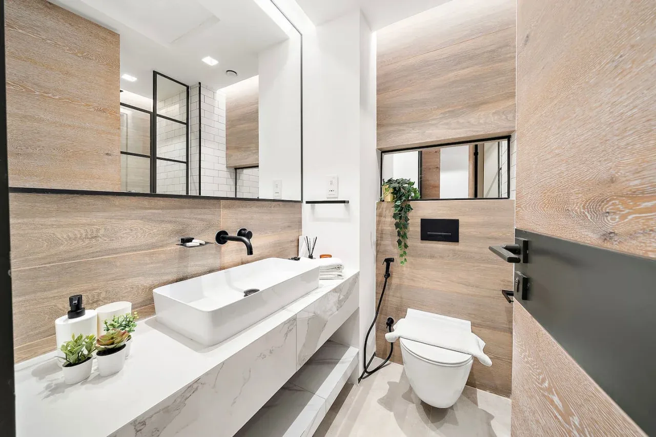 Un baño luminoso con un lavabo largo, espejo e inodoro.