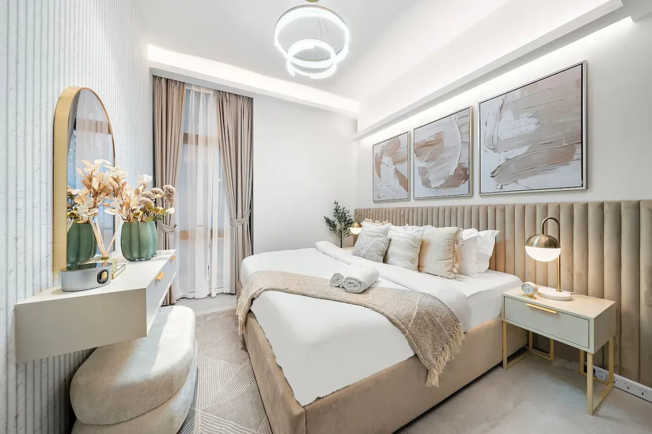 Un dormitorio luminoso con una cama bien tendida y cuadros sobre el cabecero.