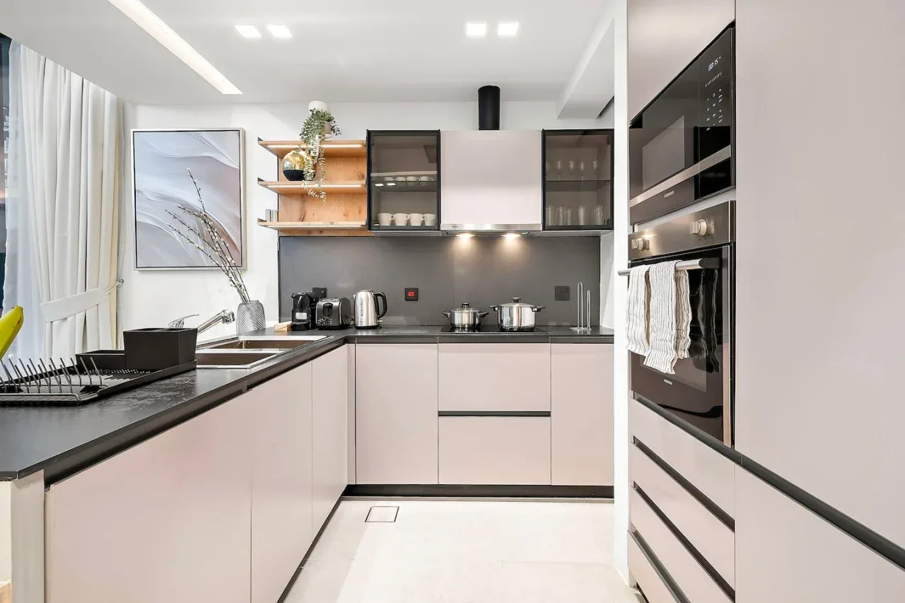 Una cocina moderna y luminosa con gabinetes claros, encimeras oscuras y electrodomésticos de acero inoxidable.