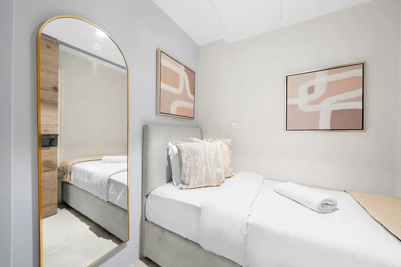 Un dormitorio luminoso con una cama bien tendida y arte abstracto en la pared.