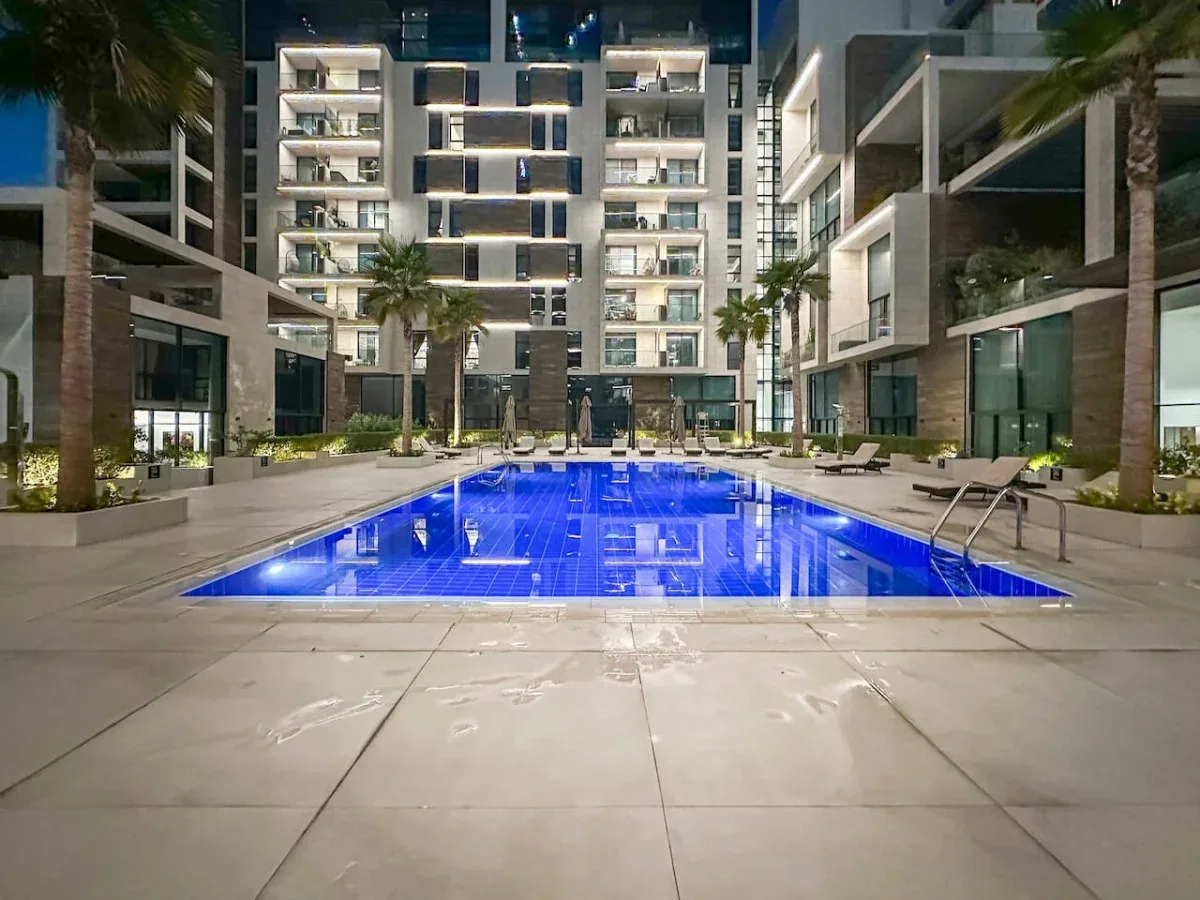 Una piscina iluminada se encuentra entre edificios de apartamentos modernos por la noche.