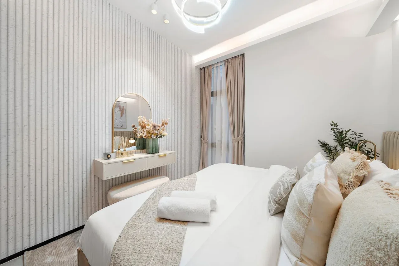 Un dormitorio luminoso cuenta con una cama bien tendida y un pequeño tocador.