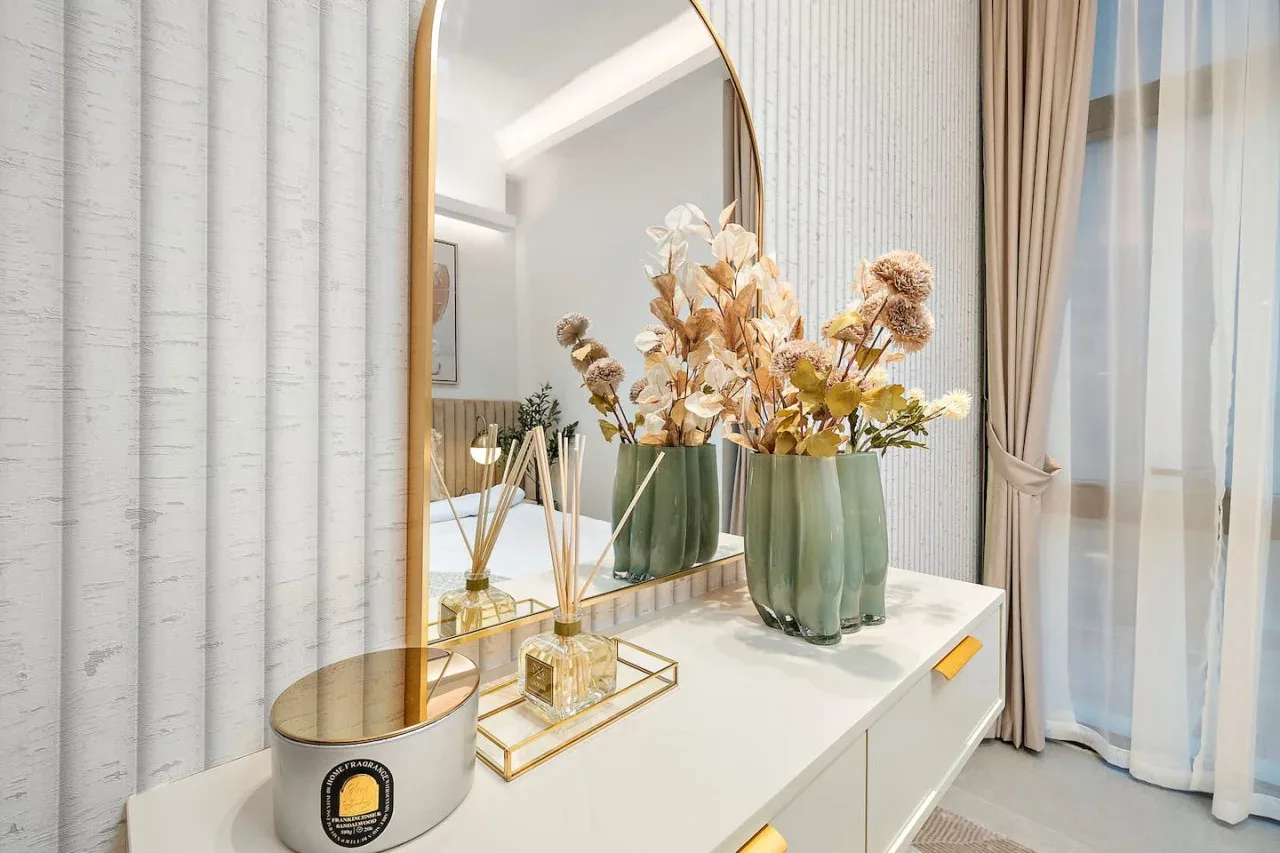 Una habitación luminosa con una cómoda blanca, jarrones decorativos y un espejo alto.
