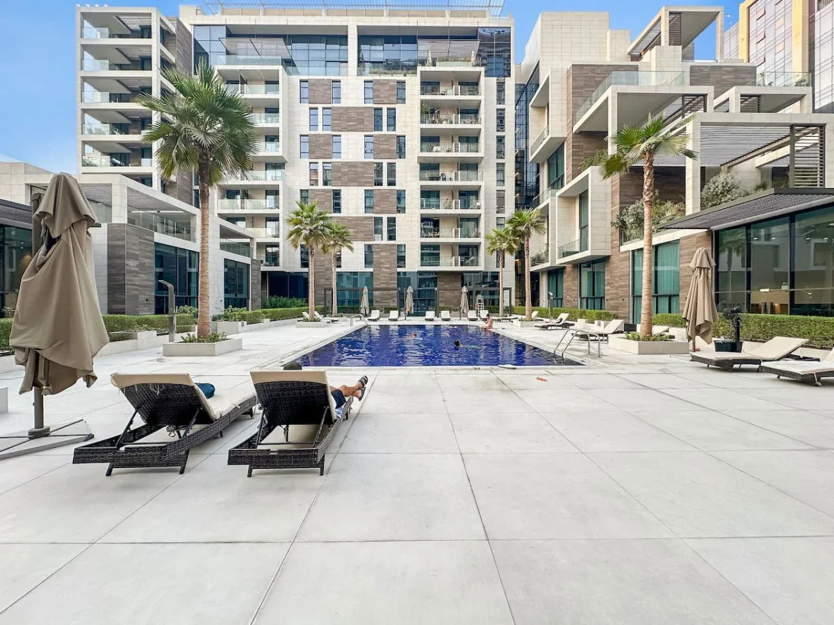 Una piscina está en un patio rodeado de edificios modernos y asientos para descansar.