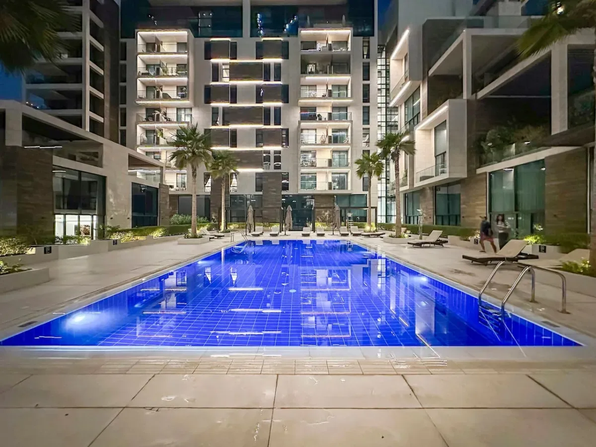 Una piscina iluminada de azul está en un patio rodeado de edificios modernos.