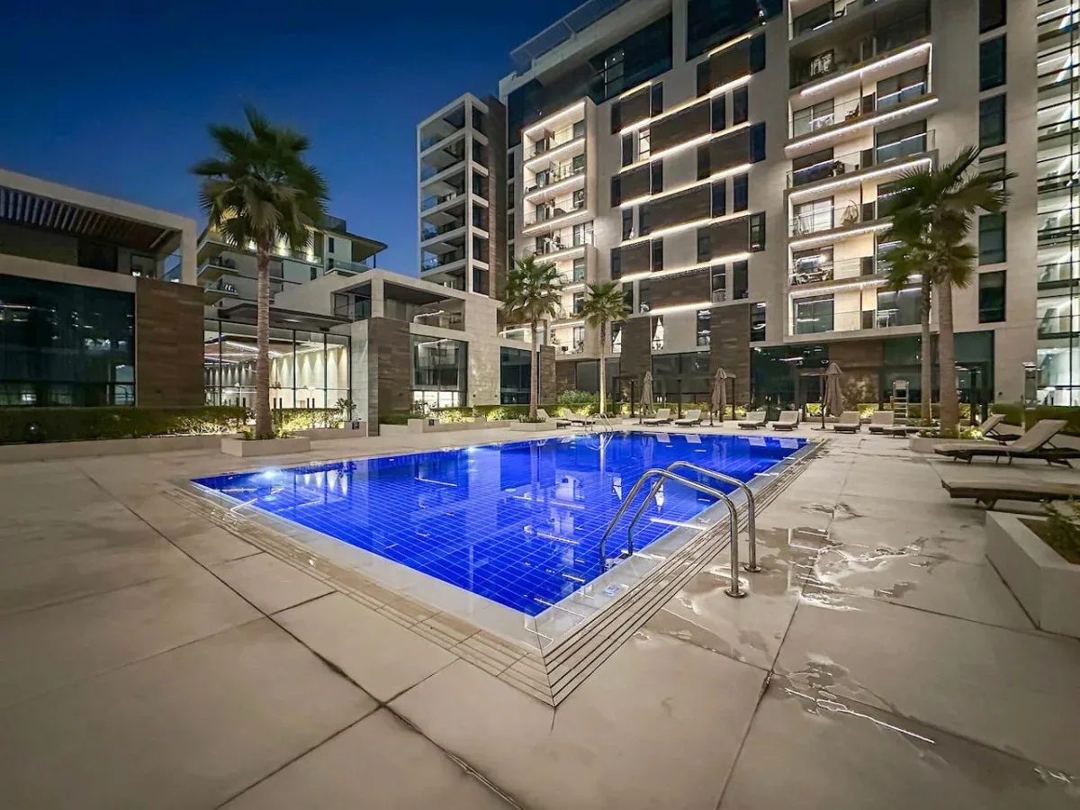 Una piscina exterior iluminada está rodeada de edificios de apartamentos modernos al anochecer.