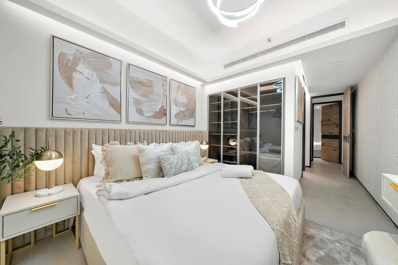 Un dormitorio luminoso con una cama, una mesita de noche y un armario con puertas de vidrio.