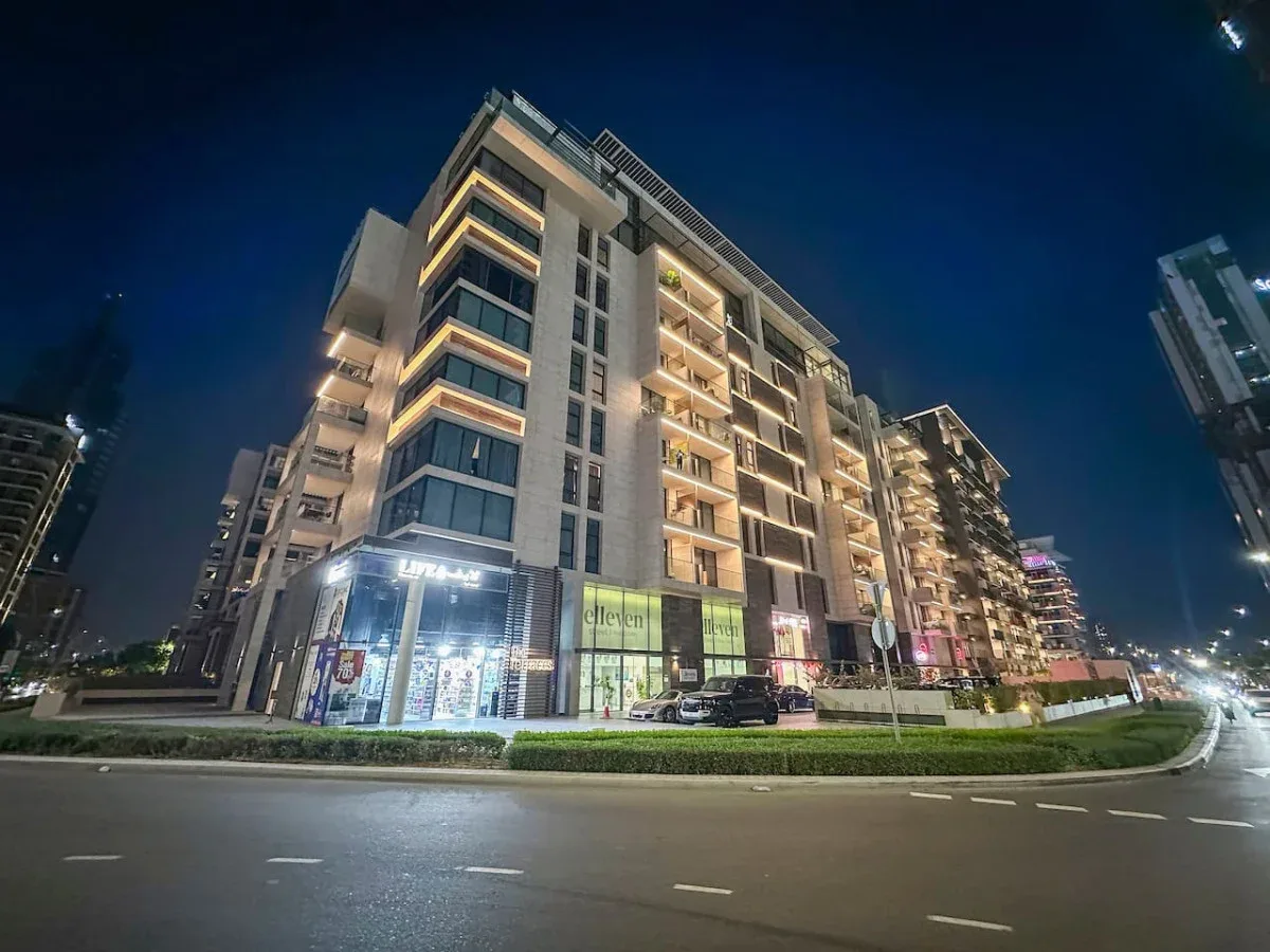 Un edificio de apartamentos moderno con balcones iluminados junto a una calle de la ciudad por la noche.