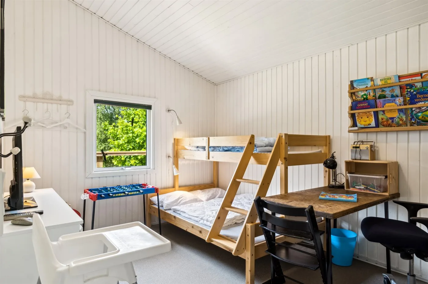 Un dormitorio luminoso con literas, un escritorio y una ventana con vistas a la vegetación.