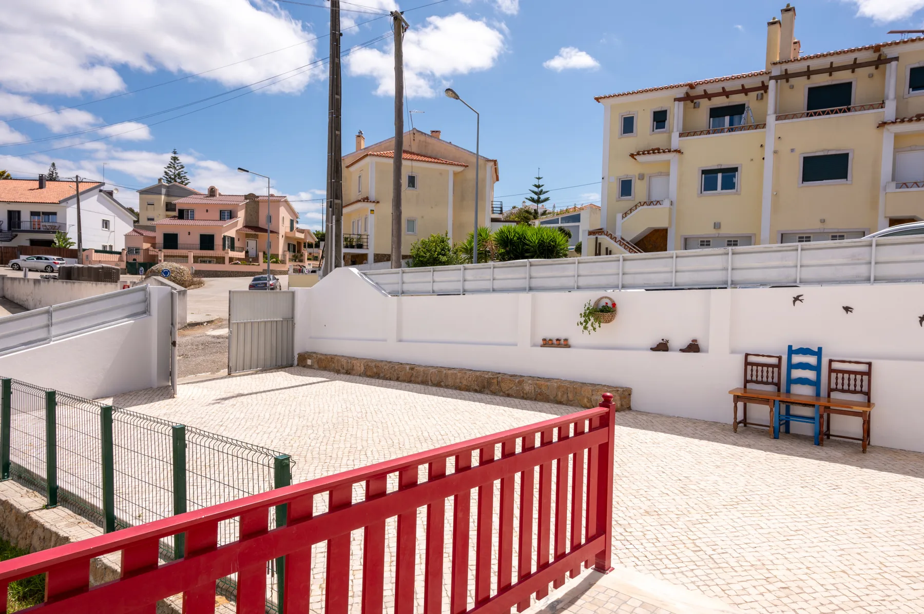 A paved outdoor courtyard is enclosed by white walls and a red railing.