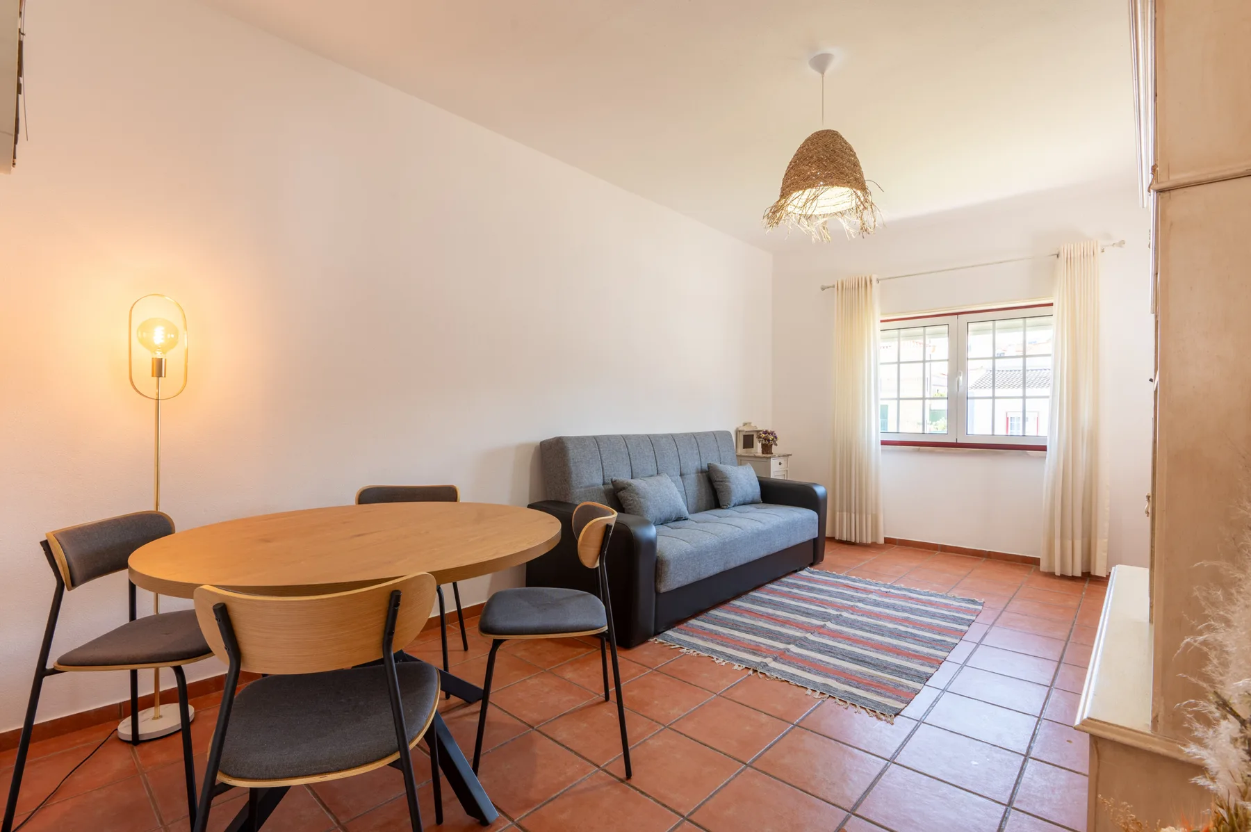 A living and dining area with a gray sofa, wooden table, and window.
