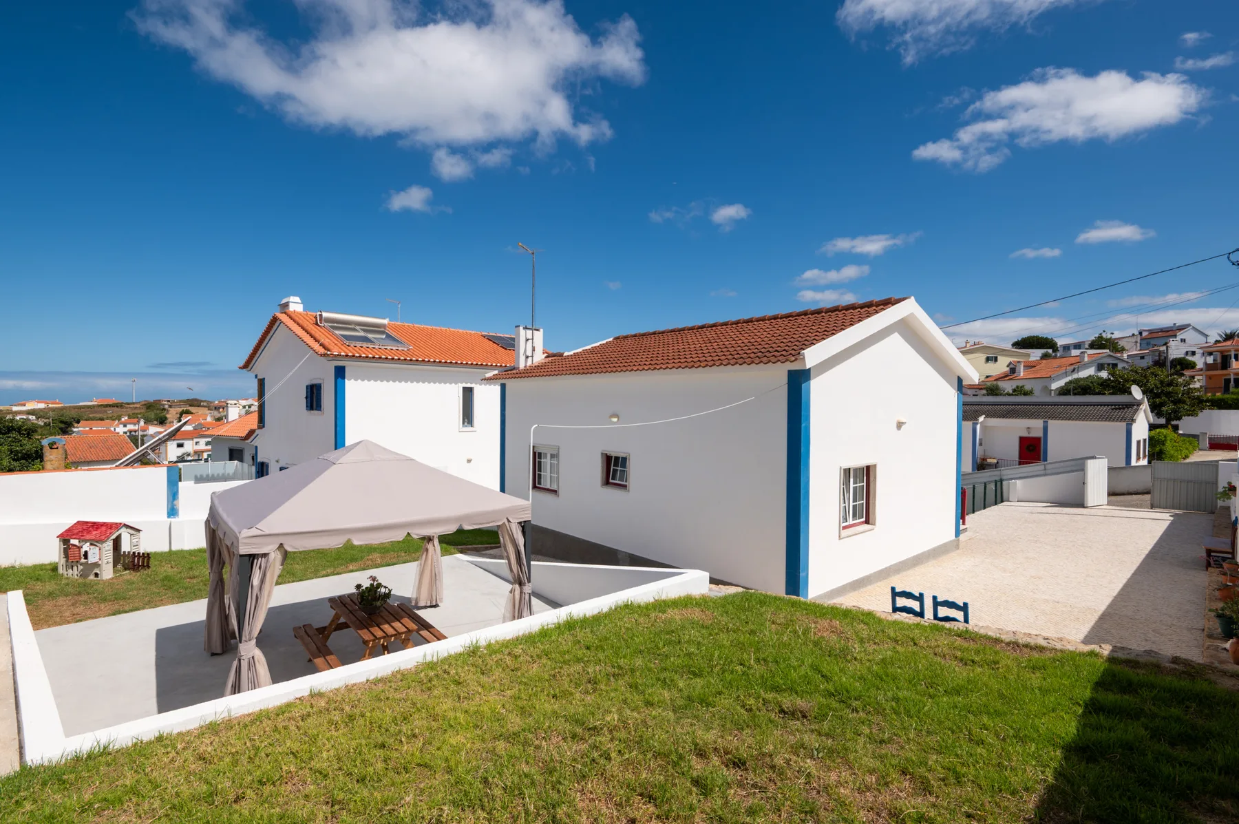 A white house with red-tiled roofs and a covered outdoor seating area.