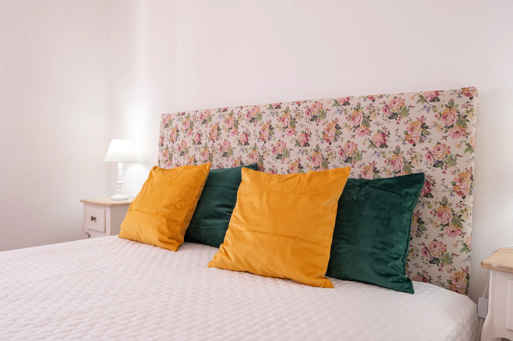 A bedroom with a floral headboard and colorful pillows on the bed.