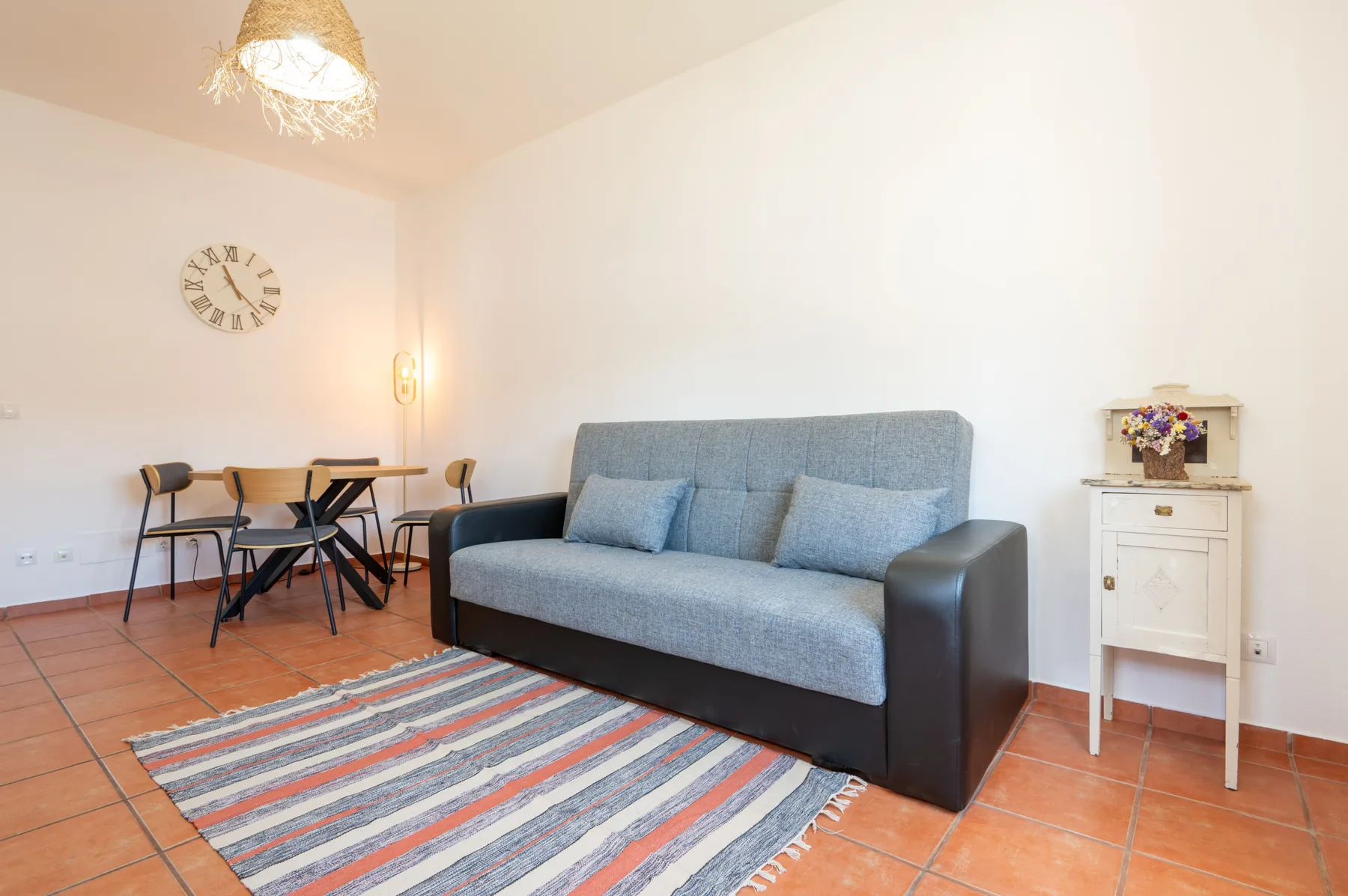 A living room with a sofa, a small dining table, and a striped rug.