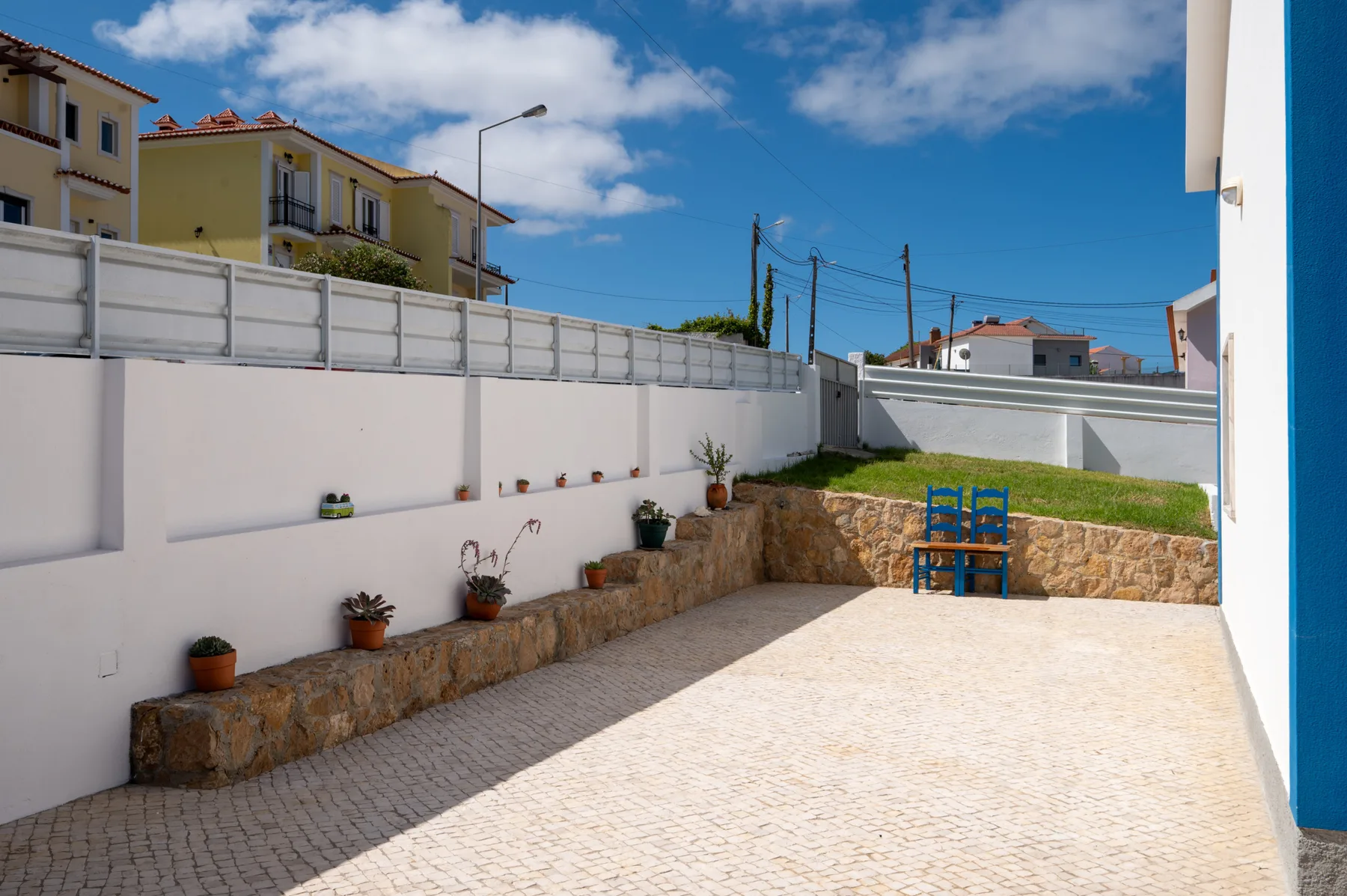A paved outdoor terrace with stone-edged planters and a blue chair.