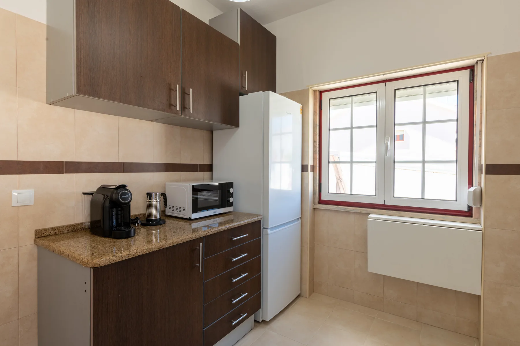 A kitchen with dark cabinets, a refrigerator, and a window.