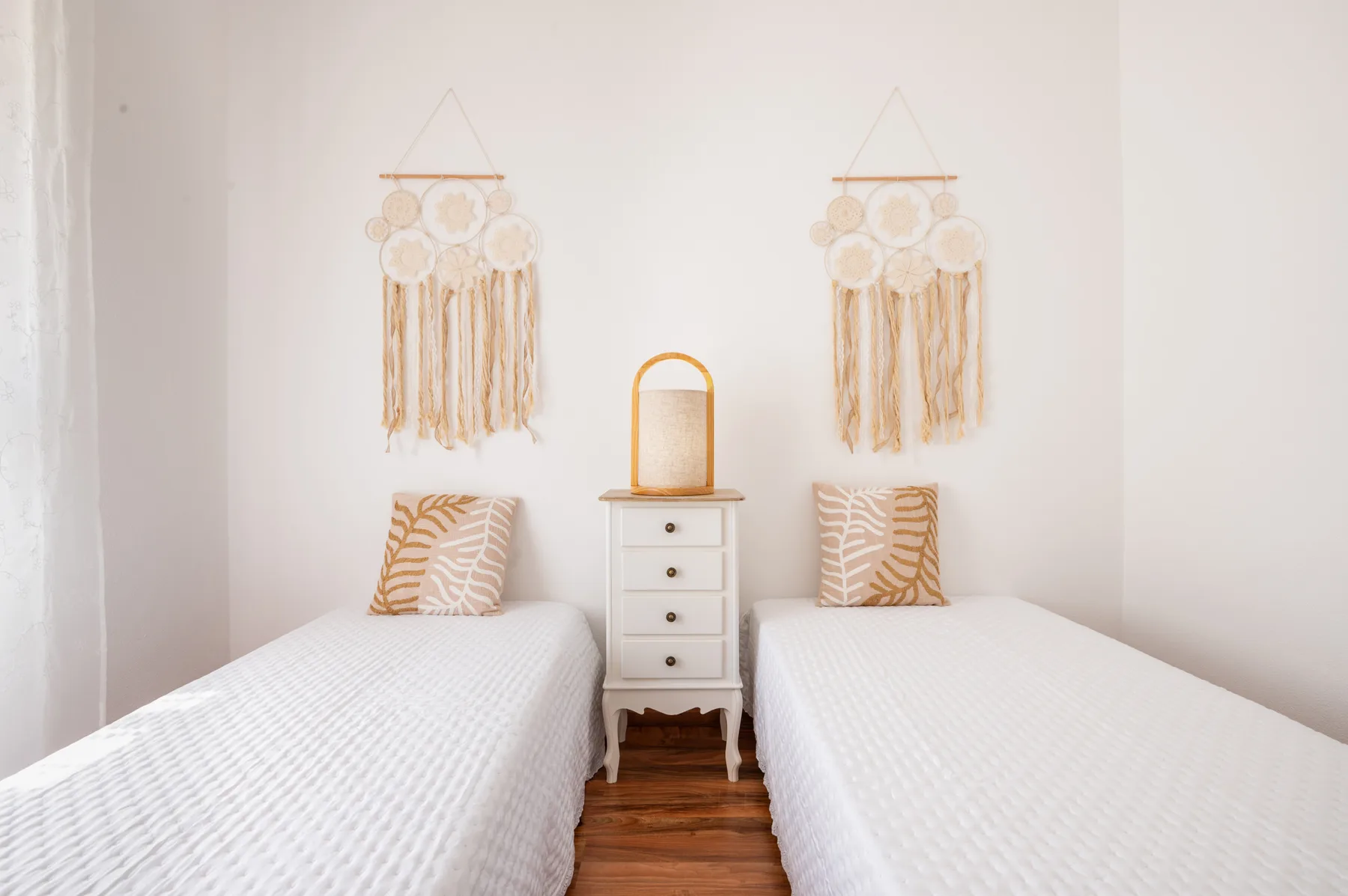 A bright bedroom with two single beds and decorative wall hangings.
