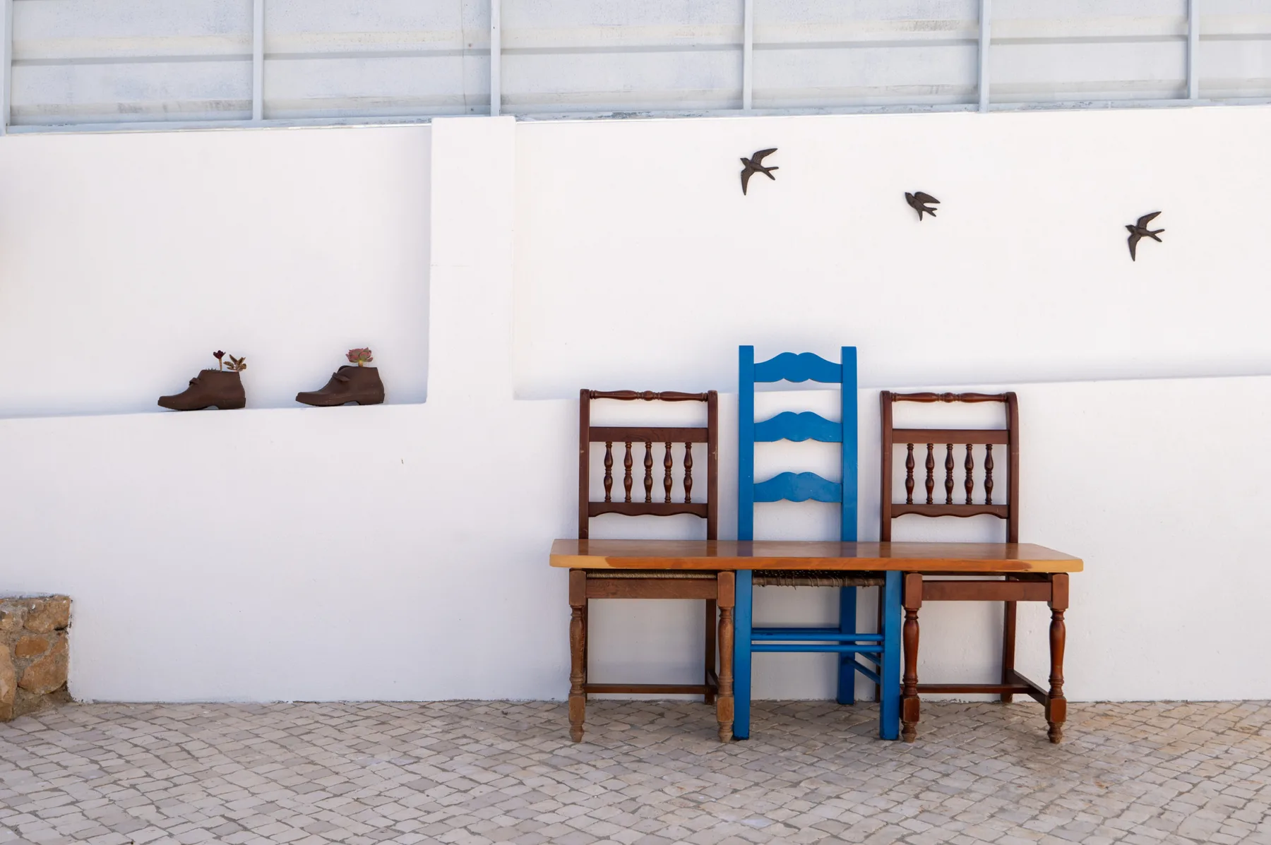 An outdoor seating area with a table and chairs against a white wall.