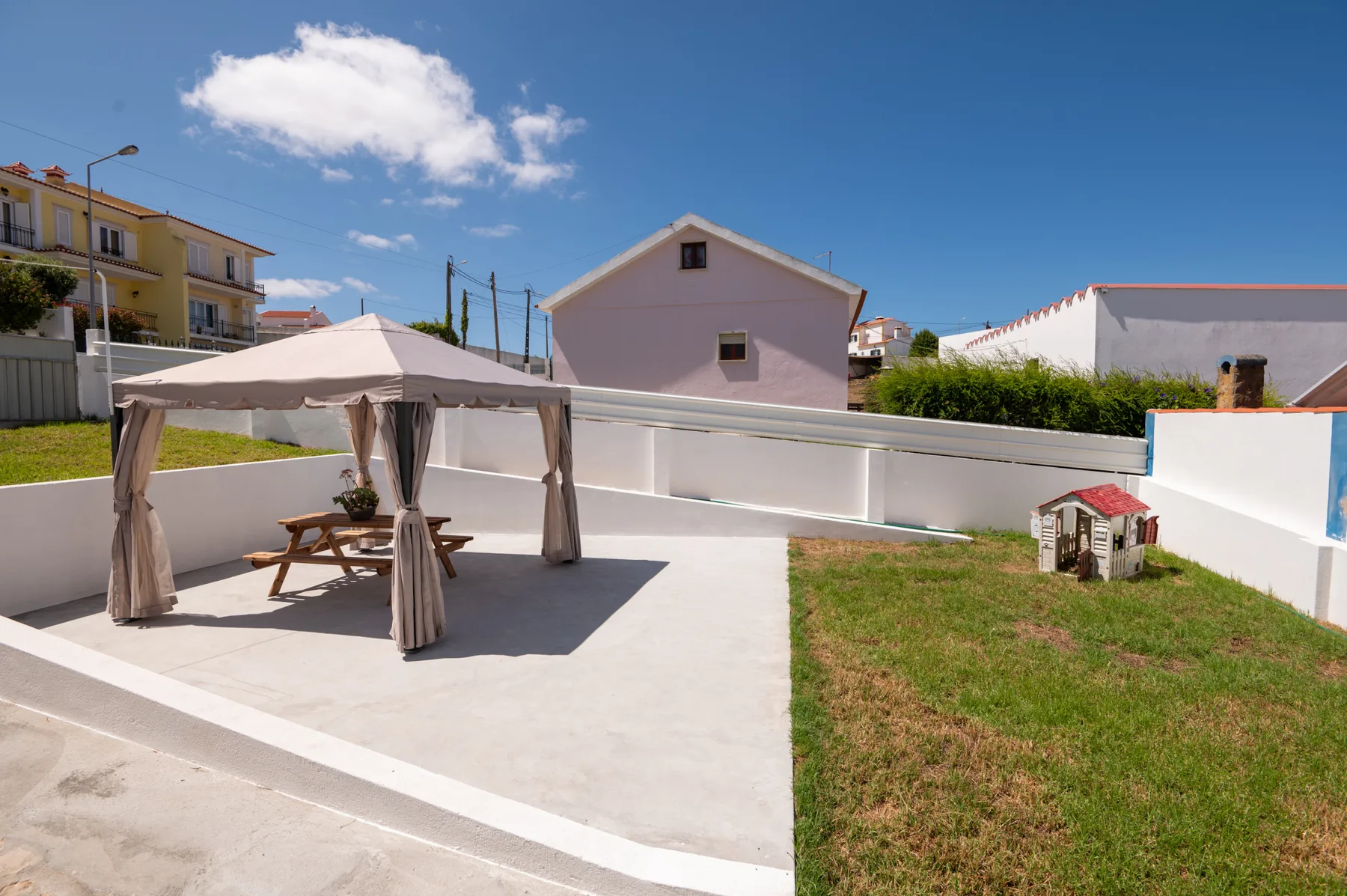 A sunny patio with a covered seating area and a patch of grass.