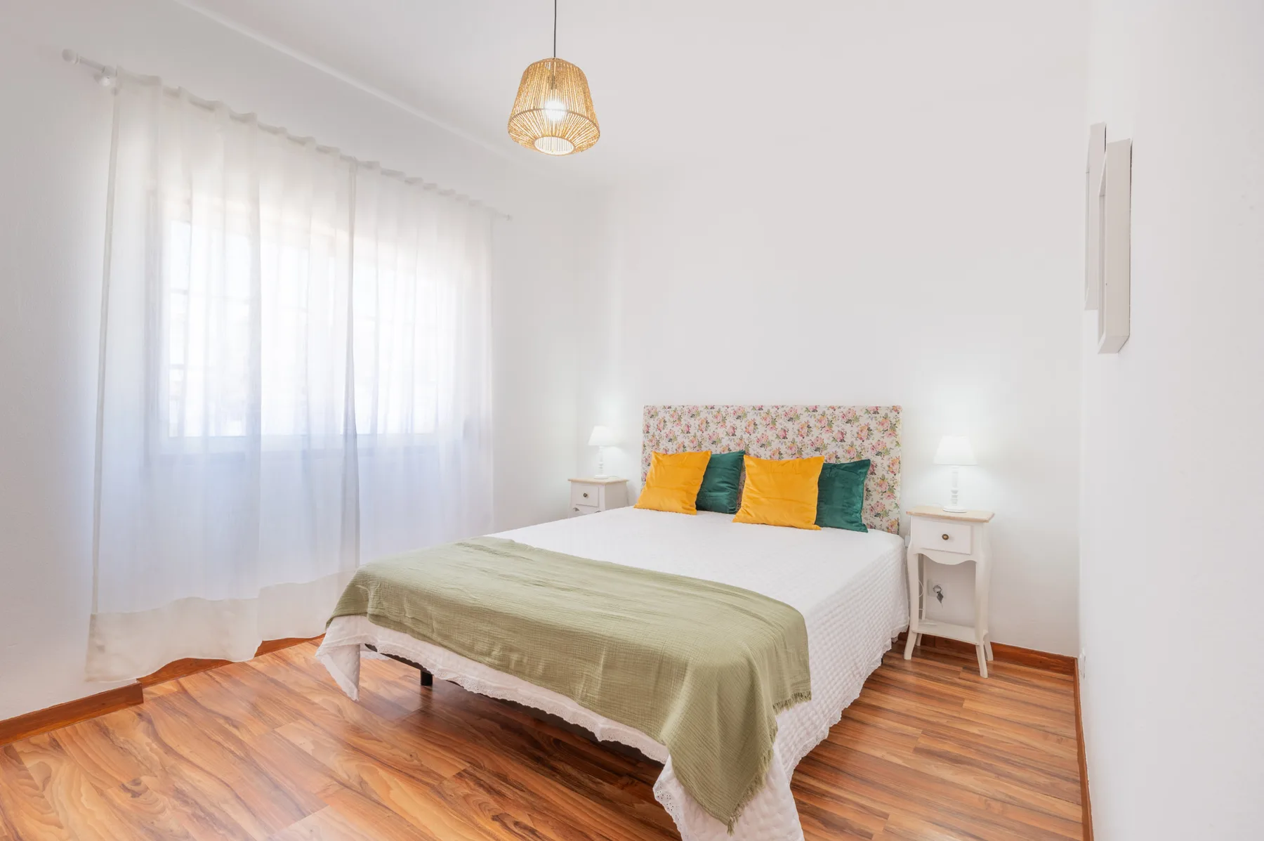 A bright bedroom with a bed beneath a woven pendant light.