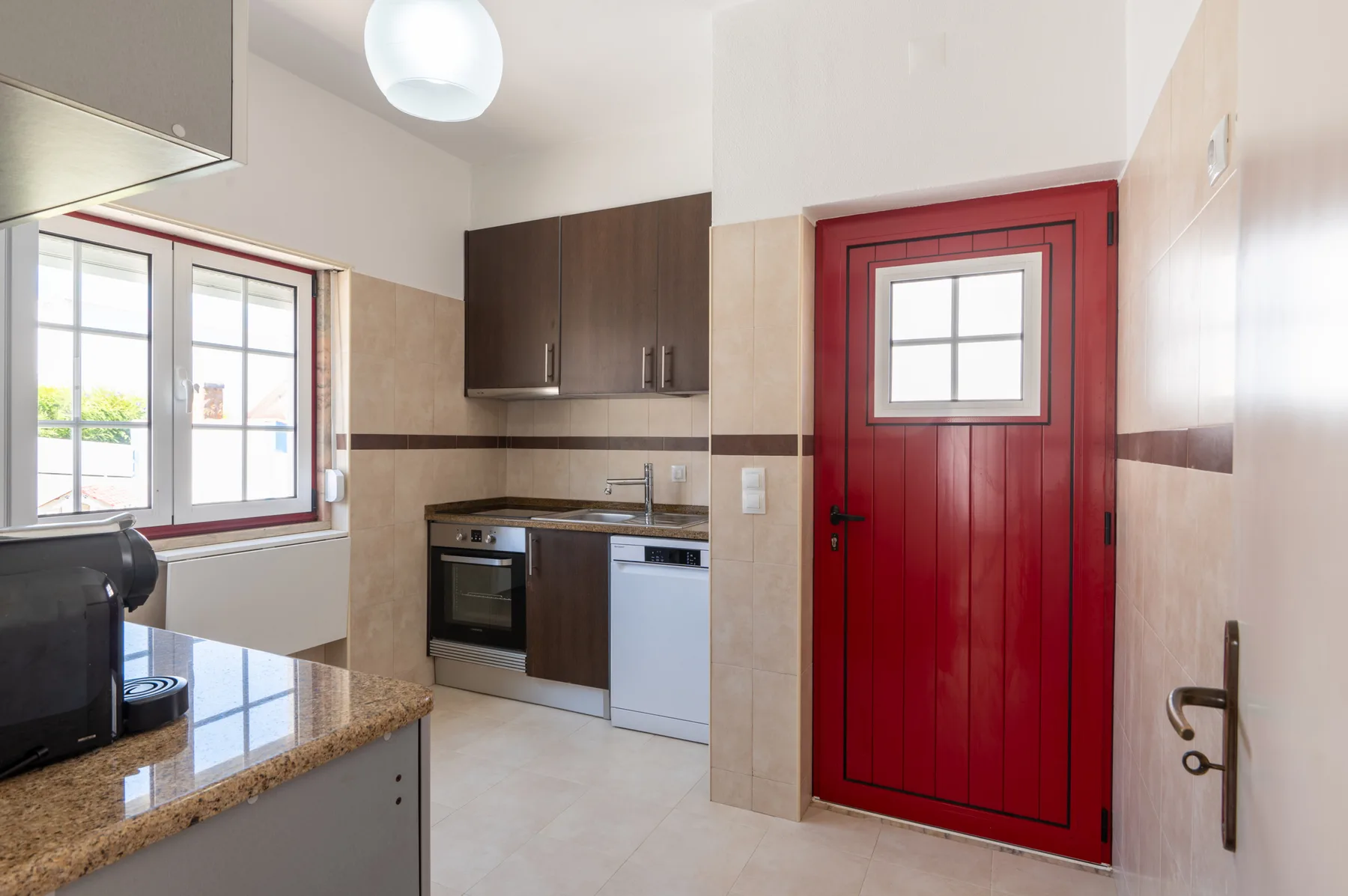A kitchen with a red door, tiled walls, and a countertop.