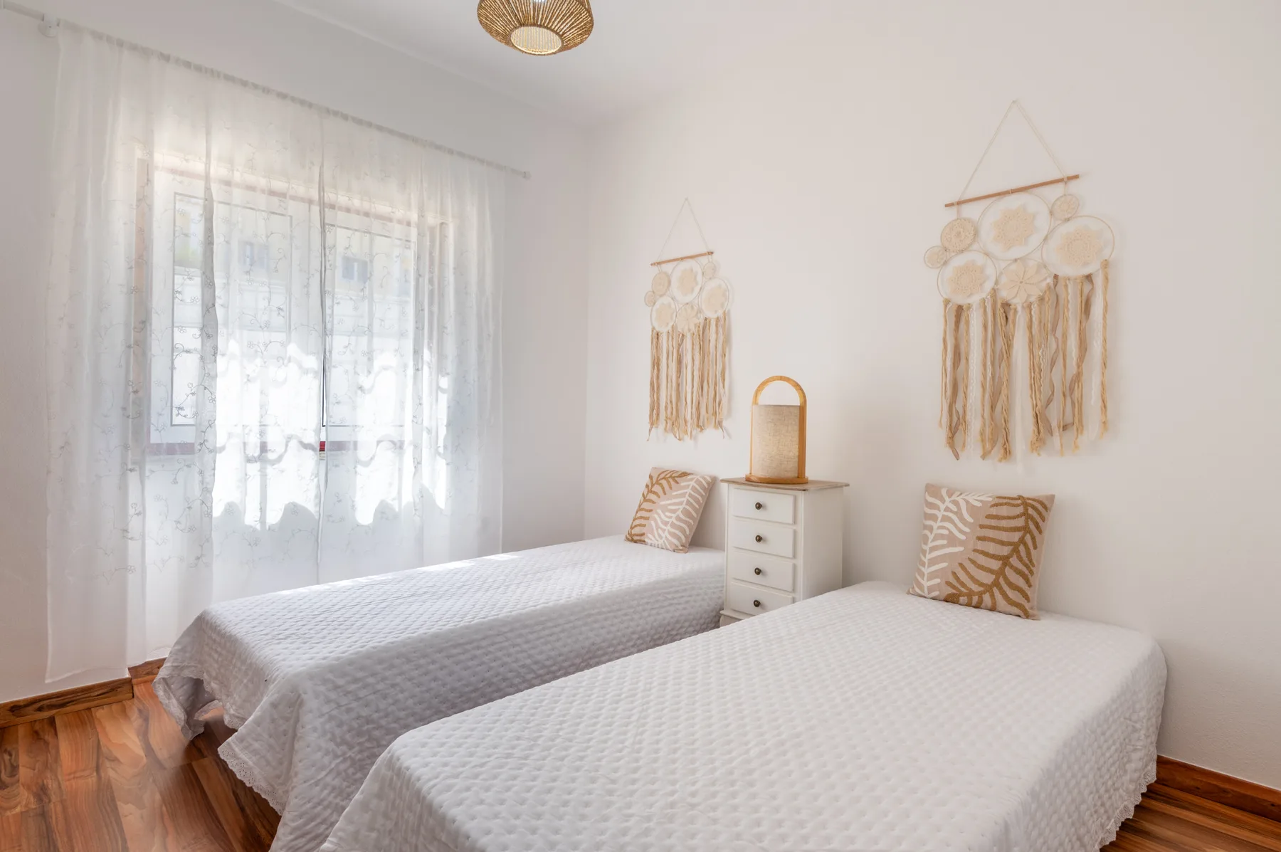 A bright bedroom with two single beds and decorative wall hangings.