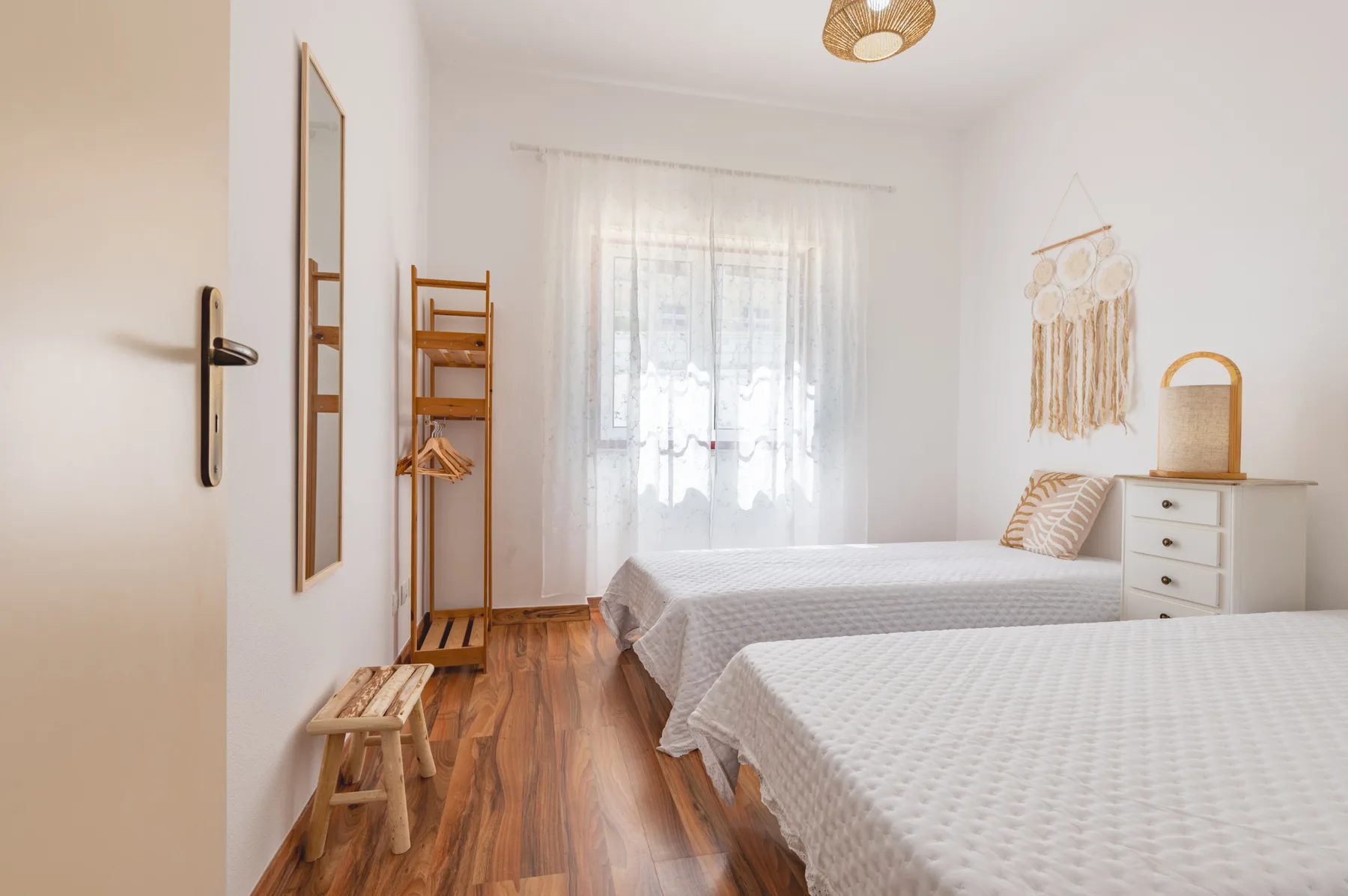 A bright bedroom with two beds, a window, and wooden flooring.