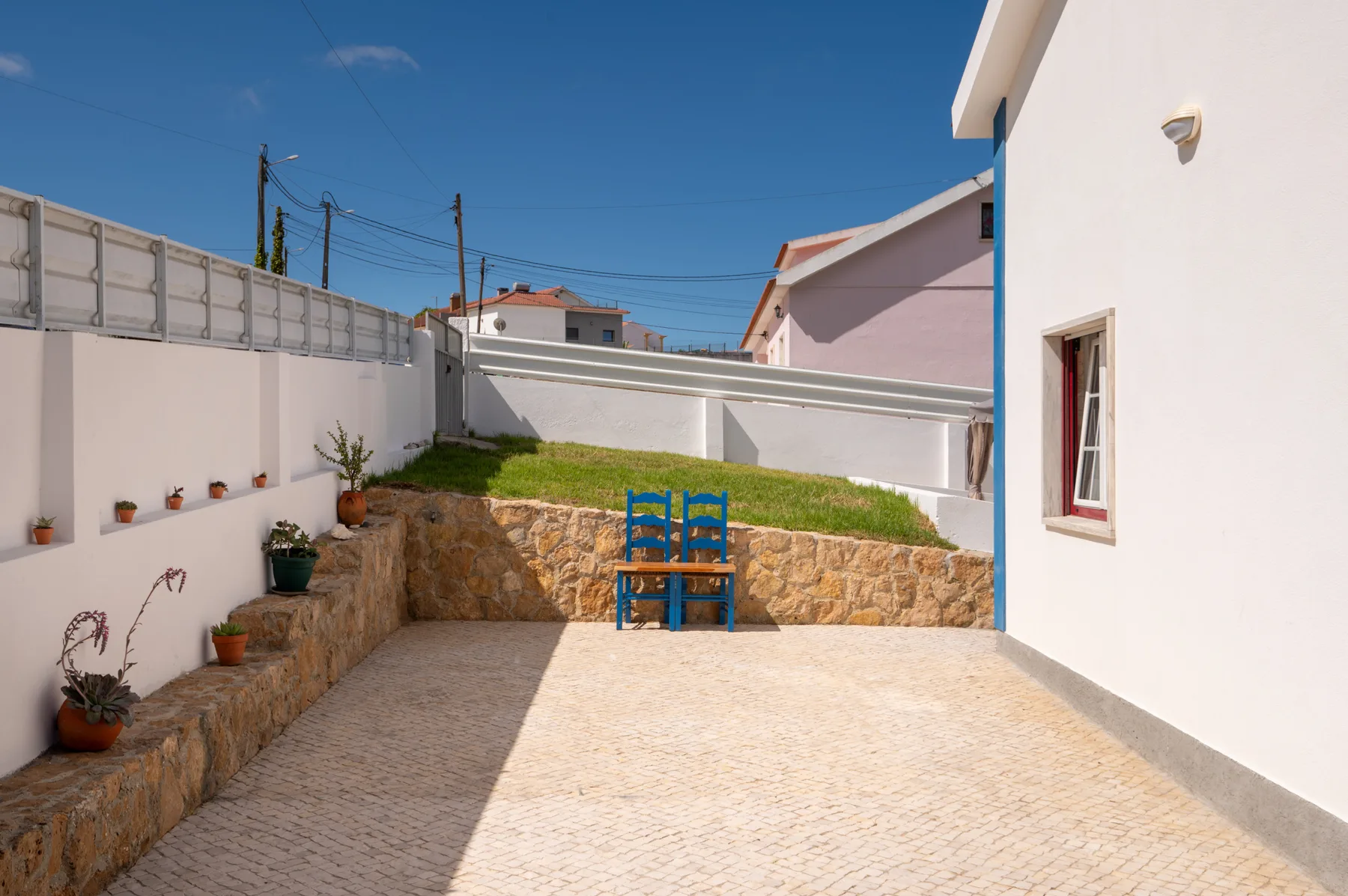 A paved courtyard with a raised garden bed and blue chairs.