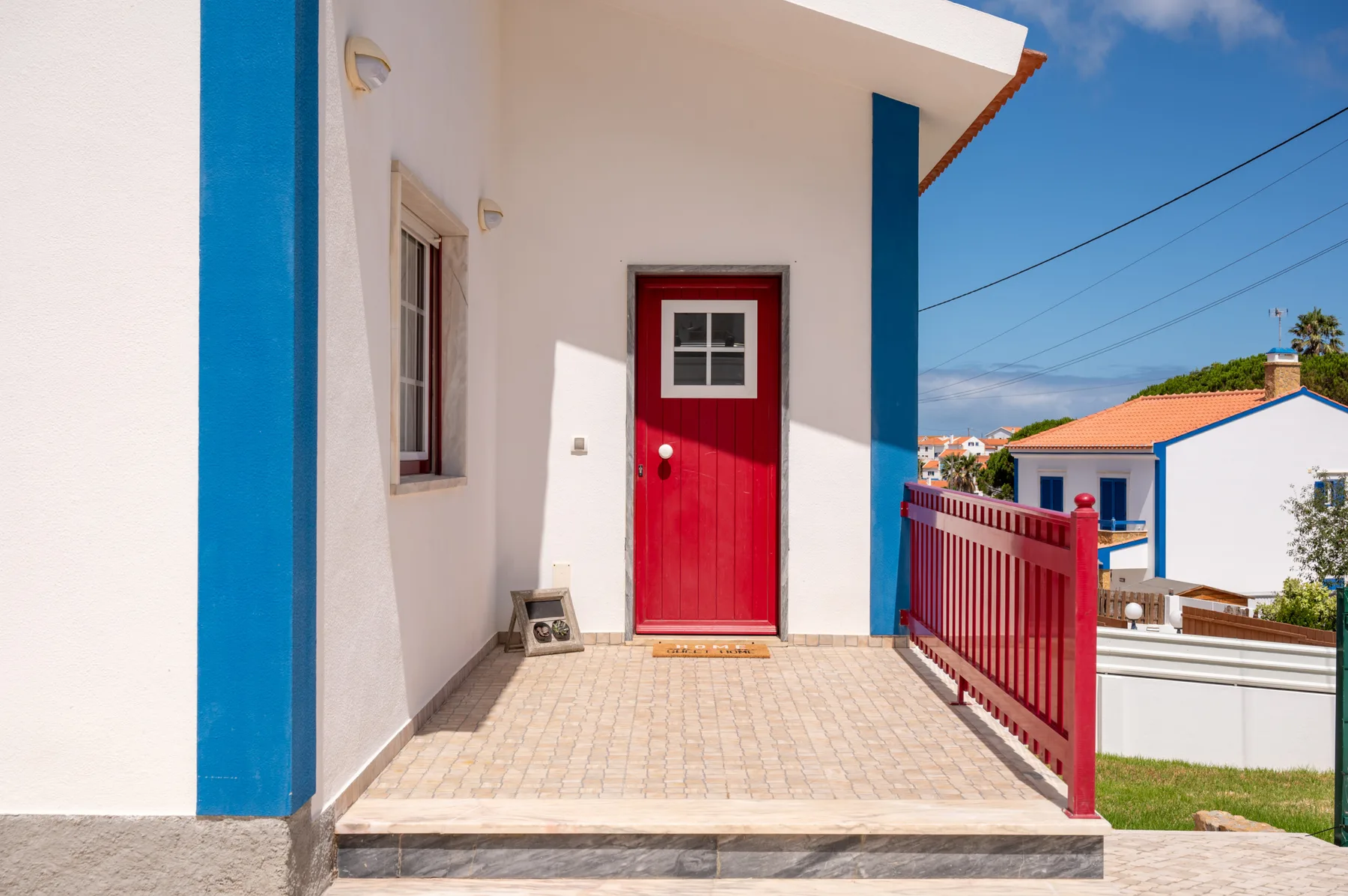 A tiled entrance patio with a red door and red railing.