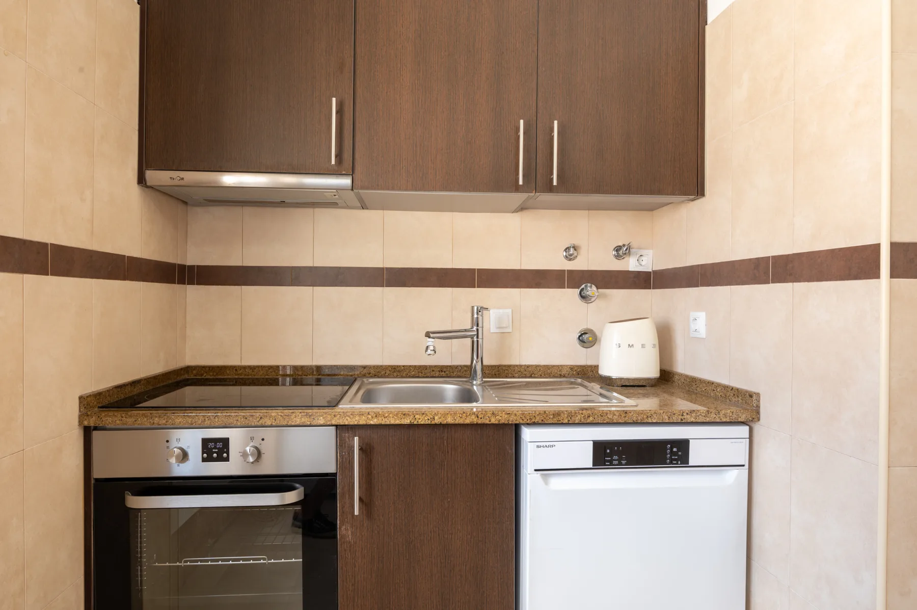 A kitchen with dark cabinets, a countertop, sink, oven, and dishwasher.