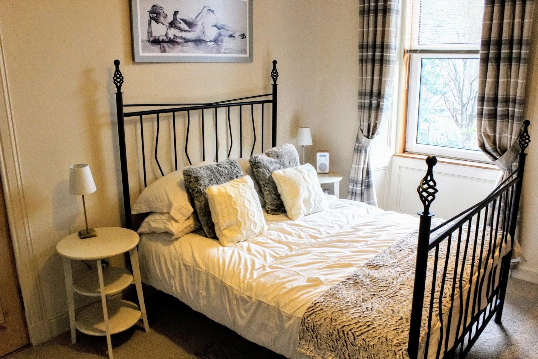 A bedroom with a neatly made bed and a window framed by plaid curtains.